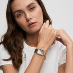 Tamaris The Square Damenuhr in Gold mit rechteckigem Gehäuse, schwarzem Zifferblatt und goldenem Gliederarmband am Handgelenk getragen